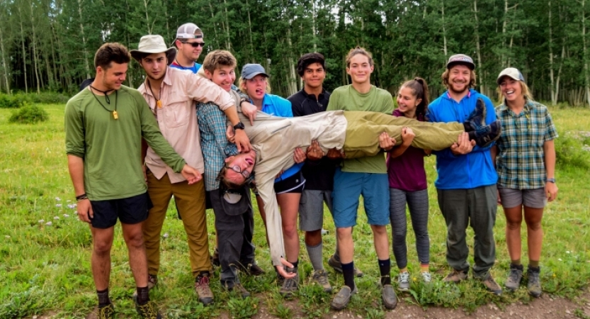 a group of gap year students hold up one person who is laying across their hands